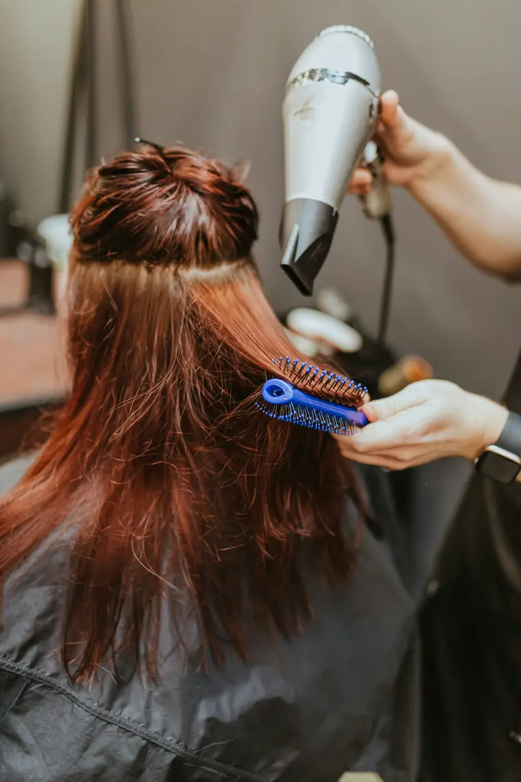 Coiffeuse réalisant un brushing sur une chevelure rousse