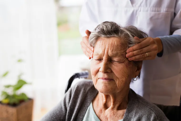 Praticienne posant les mains sur les tempes d’une patiente âgée